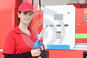 Portrait of happy smiling beautiful woman gas station attendant in red uniform holding a fuel petrol pump nozzle against at gas