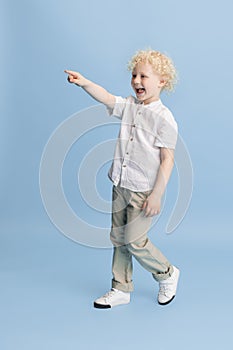 Portrait of happy smiling boy posing isolated over blue studio background.