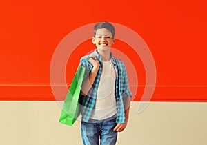 Happy smiling boy teenager with shopping bag in the city on red background