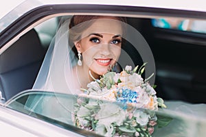 Portrait of the happy smiling bride with the wedding bouquet sitting in the car.