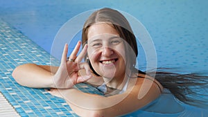 Portrait of happy smiling brunette woman relaxing in swimming pool and showing OK sign with fingers.