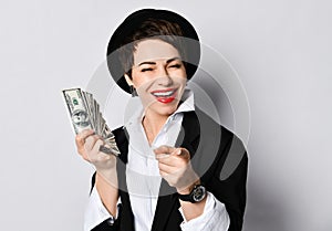 Portrait of happy smiling business woman holding fan of dollars banknotes, pointing finger and winking at us