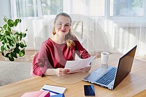 Portrait of happy smiling business woman sitting at wooden desk with laptop and working with documents at home office, copy space