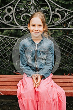 Portrait happy smiling candid eight year old kid girl face sits on bench in nature. prepubertal age of children and their lives, m