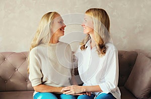 Portrait of happy smiling caucasian middle aged mother and adult daughter looking at each other together sitting on couch at home