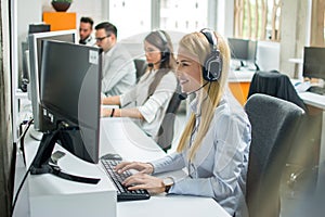 Portrait of happy smiling cheerful support phone operator in headset working on computer in call center.