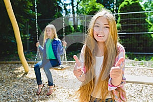 Portrait of happy and smiling child show thumb up at park. On the background other girl riding a swing