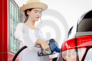 Portrait of happy smiling customer woman holding fuel petrol pump nozzle against for filling up her car, beautiful young lady