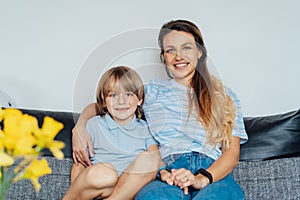 Portrait of happy smiling family at home. Son and mother sitting on the sofa and looking at camera, hugging each other