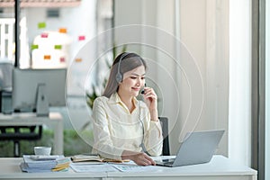 Portrait of happy smiling female customer support phone operator at workplace. Asian