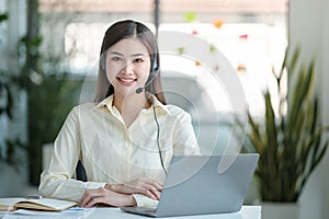 Portrait of happy smiling female customer support phone operator at workplace. Asian