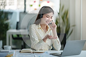 Portrait of happy smiling female customer support phone operator at workplace. Asian