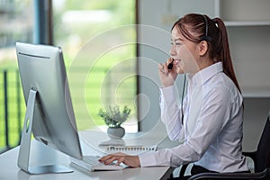 Portrait of happy smiling female customer support phone operator at workplace. Asian