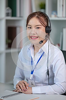 Portrait of happy smiling female customer support phone operator at workplace. Asian