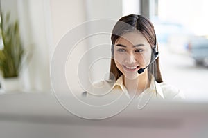 Portrait of happy smiling female customer support phone operator at workplace. Smiling beautiful Asian woman working in