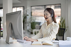 Portrait of happy smiling female customer support phone operator at workplace. Smiling beautiful Asian woman working in