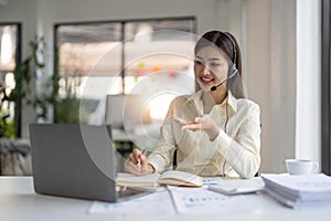 Portrait of happy smiling female customer support phone operator at workplace. Smiling beautiful Asian woman working in