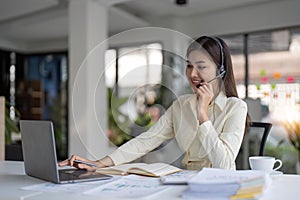 Portrait of happy smiling female customer support phone operator at workplace. Smiling beautiful Asian woman working in
