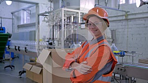 Portrait of happy smiling Female Engineer into helmet and coveralls at work near conveyor line