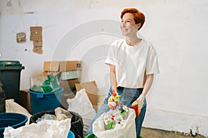 Portrait of happy smiling female worker in latex gloves sorting diverse plastic garbage for further disposal at modern