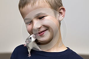 Portrait of happy smiling funny cute handsome child boy with white pet mouse hamster on shoulder on light copy space background.