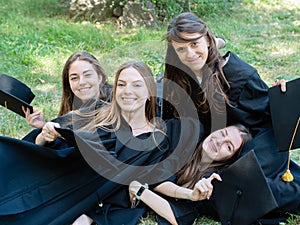 Portrait of a happy smiling girl in a black robe lying on the grass. A young woman is celebrating her graduation. New