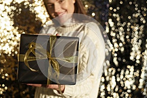 Portrait of a happy smiling girl holding a golden gift box on a golden background.