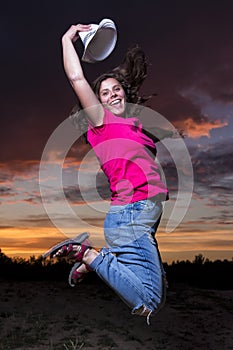 Portrait of happy smiling girl jumping in the evening against colorful sky background with clouds at sunset