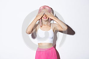 Portrait of happy smiling girl in pink anime wig and halloween outfit, close eyes with hands and waiting for surprise