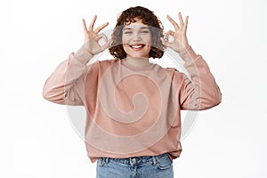 Portrait of happy smiling girl shows approval, agrees with you, okay OK sign, praise and compliment, say yes, standing