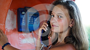 Portrait of happy and smiling girl talking in the phone booth on the city street