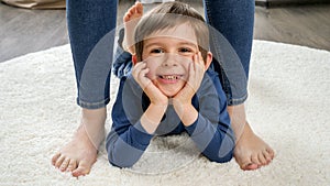 Portrait of happy smiling little boy lying on carpet between mother's feet