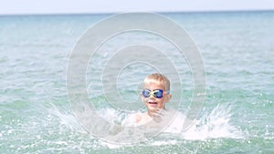 Portrait happy smiling little boy playing in ocean sea water, child having fun, swimming and splashing. Summer vacation