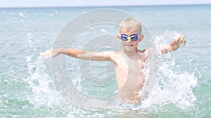 Portrait happy smiling little boy playing in ocean sea water, child having fun, swimming and splashing. Summer vacation