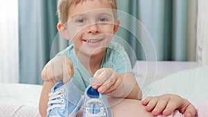 Portrait of happy smiling little boy playing with small baby boots and pregnant mother lying on bed at home. Concept of