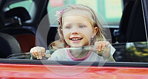 Portrait of happy smiling little child passenger sitting in red car