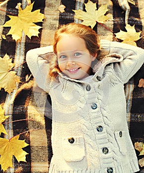 Portrait happy smiling little girl child lying having fun with yellow maple leafs in sunny autumn day top