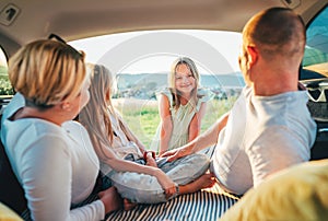 Portrait of happy smiling little girl gazing at camera. Happy young couple with two daughters inside the car trunk during auto