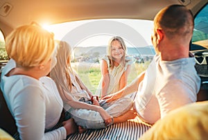 Portrait of happy smiling little girl gazing at camera. Happy young couple with two daughters inside the car trunk during auto