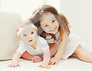 Portrait happy smiling little older and younger sisters together, children playing in white room at home