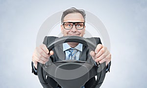 Portrait of a happy smiling man in a dark jacket, glasses and tie turning the steering wheel on a smoky light background