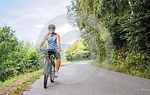 Portrait of a happy smiling man dressed in cycling clothes, helmet and sunglasses riding a bicycle on the asphalt out-of-town