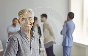 Portrait of happy smiling mature businessman standing against blurred office background