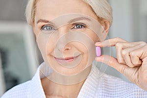 Portrait of happy smiling mid aged Caucasian woman taking pills isolated on grey.