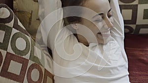 Portrait of happy smiling mixed race woman lying on couch at home at morning. Beautiful brunette female relaxing