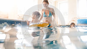 Portrait of happy smiling mother with 3 years old little son swimming in the pool at gym. Family raelaxing, having fun