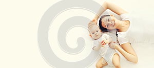 Portrait of happy smiling mother and baby lying on the floor or bed together on white background, top view