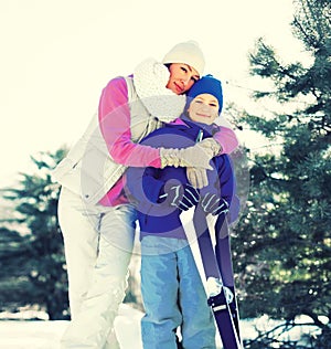 Portrait of happy smiling mother hugging child son with ski in winter forest