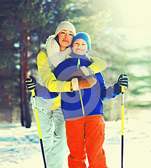 Portrait of happy smiling mother hugging child son with ski in winter forest