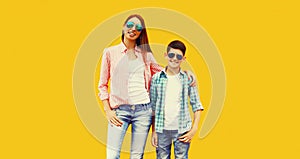 Portrait of happy smiling mother with son teenager in sunglasses, checkered shirts on yellow background